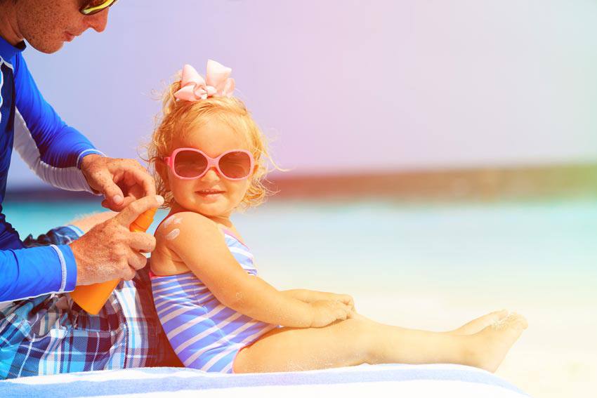 Une enfant met de la crème solaire à la plage