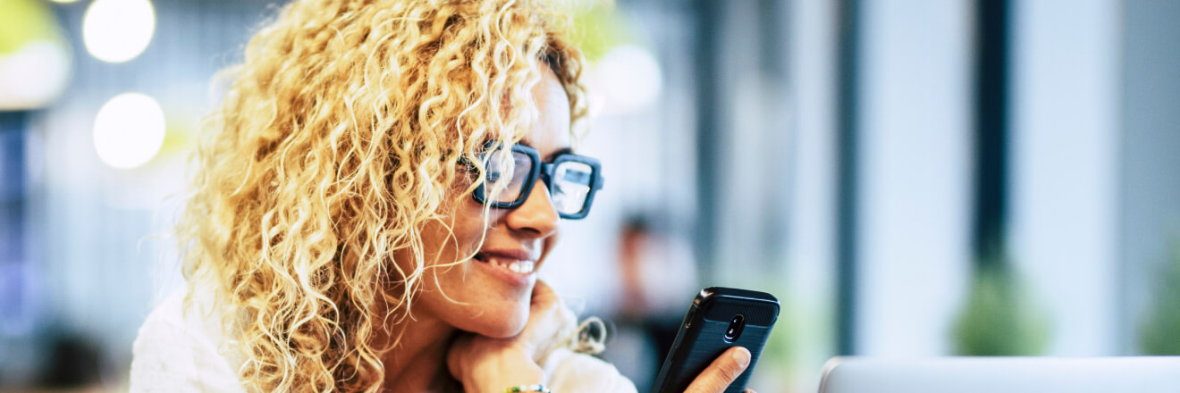 Femme sourit en regardant son téléphone cellulaire