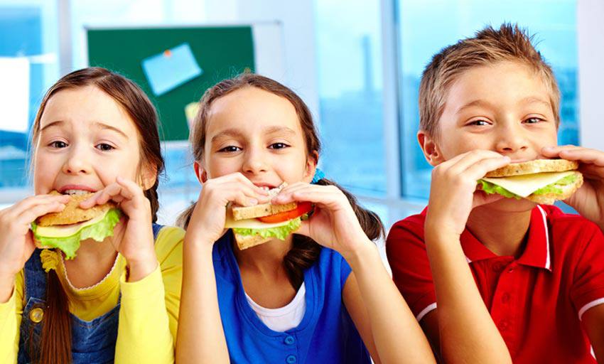 Trois petits enfants mangent des sandwichs