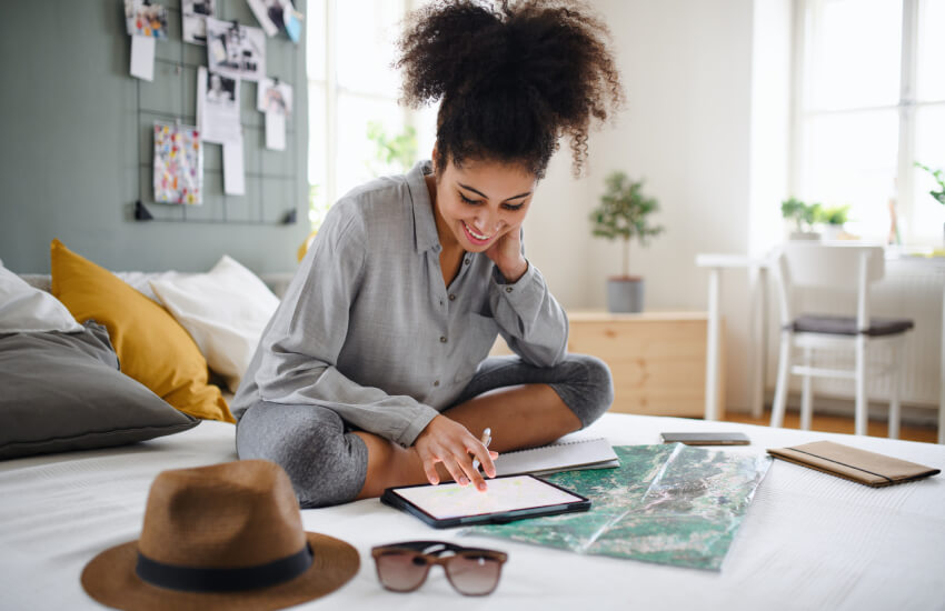 Une femme souriante assise sur son lit en train de regarder sur son cahier de notes